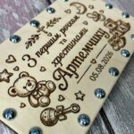 Крупний план детального гравіювання дитячих малюнків (ведмедик, брязкальце, кубики, хрестик), пам'ятного напису та справжніх металевих гвинтів на дерев'яній кришці