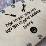 Збільшений фрагмент дерев'яної поверхні з лазерним гравіюванням напису, смайлика, інструментів та металевими гвинтами
