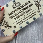 Руки тримають закриту дерев'яну коробку для грошей з гумористичним написом