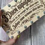 Рука тримає дерев'яну коробочку для грошей, видно її розмір і гвинти по краях