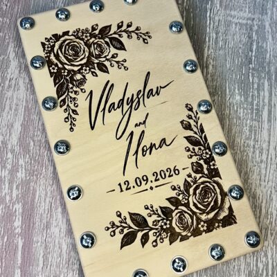Дерев'яна коробочка з гравіюванням троянд у двох кутах, рукописних імен і дати та гвинтами по краях