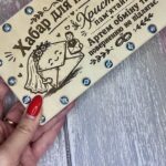 Рука тримає дерев'яну коробочку з жартівливим написом, видно гвинти по периметру